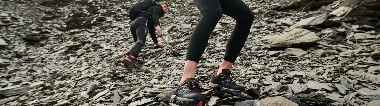 Two people hiking down a craggy surface wearing walking boots.