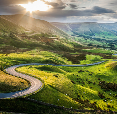 Sunset at Mam Tor, Peak District National Park, with a view along the winding road among the green hills down to Hope Valley, in Derbyshire, England.