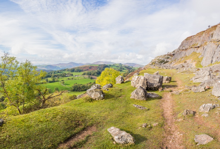 A multi image panorama of the Offas Dyke Path snaking around large boulders at the foot of cliffs on the Clwydian Range near Llangollen.