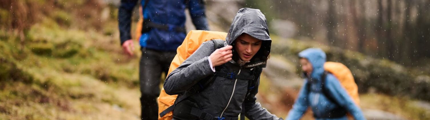 A group of three people hiking in the rain wearing waterproof jackets