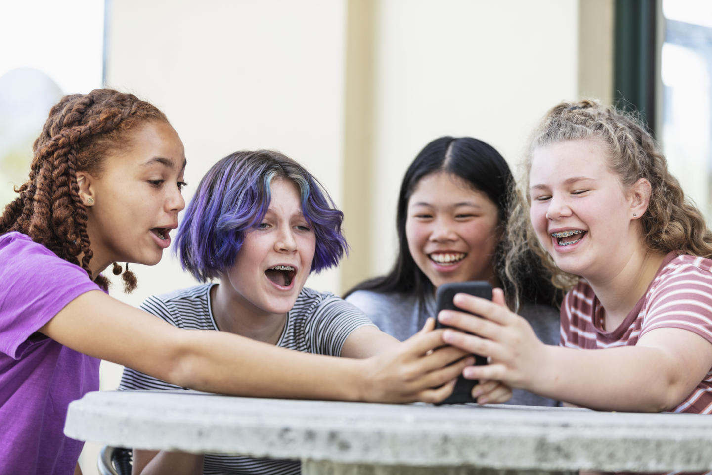 Four teenagers looking at smartphone laughing.