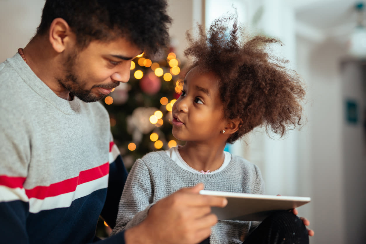 Father and child using iPad with Christmas lights in the background