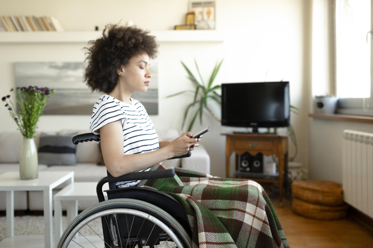 Concerned young woman in wheelchair looking at smartphone 