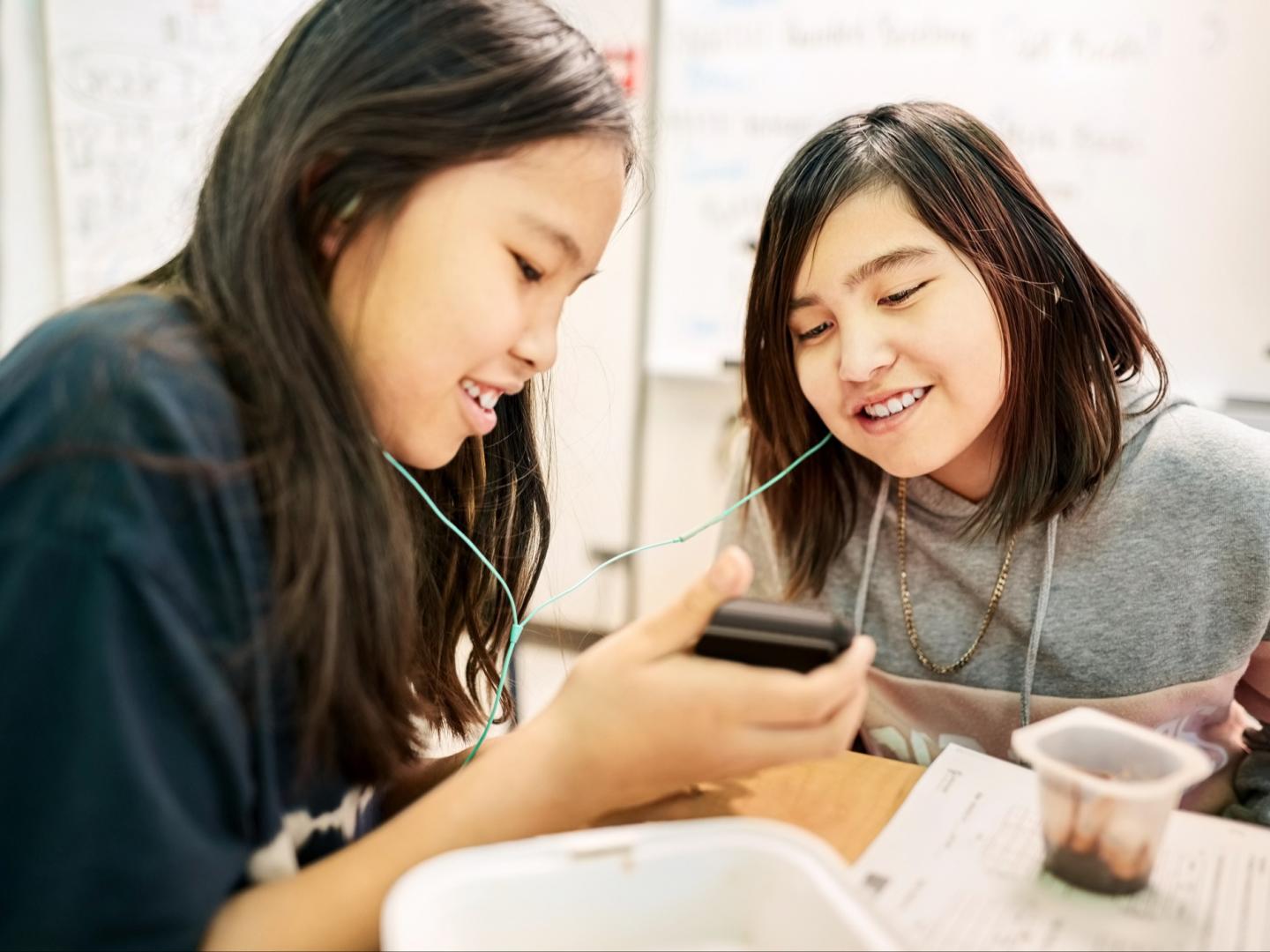 Two teens sitting in classroom using mobile phone