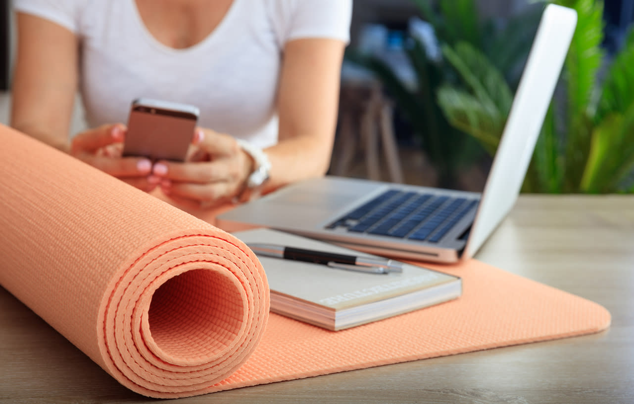 Woman at table with phone, yoga mat and notepad