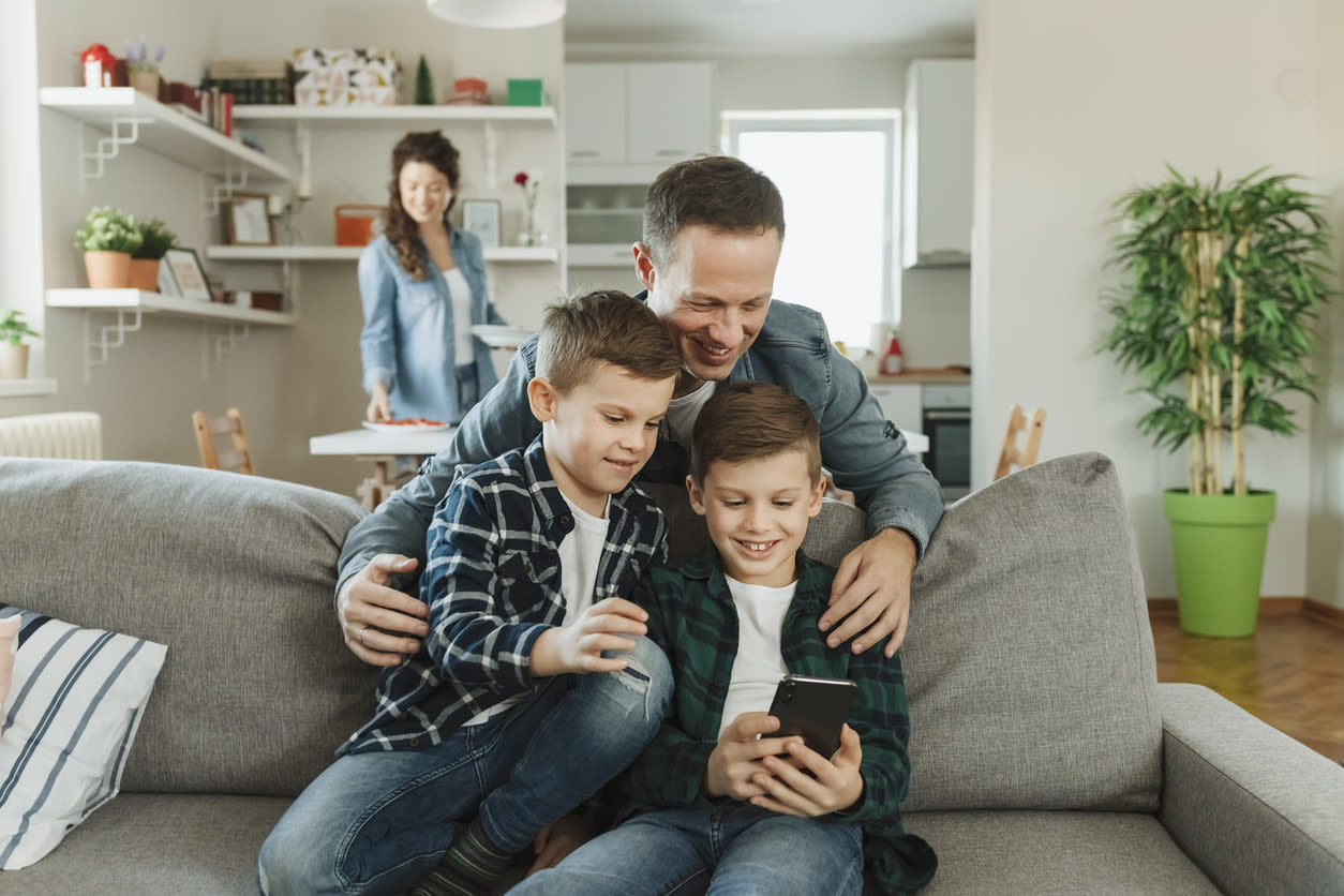 A father and two kids play with smartphones together on the couch.