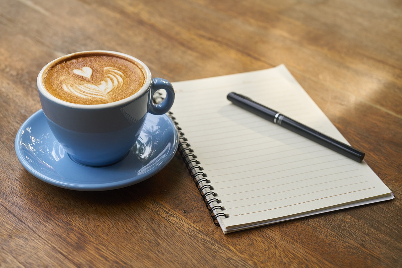 a cup of coffee and a pen on a wooden table.