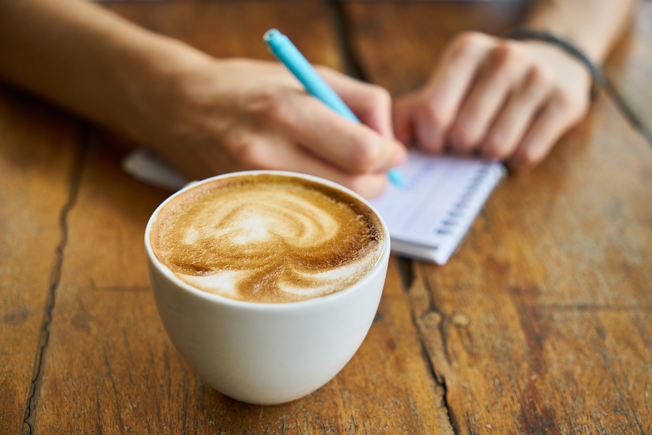 a cup of coffee and a pen on a wooden table.