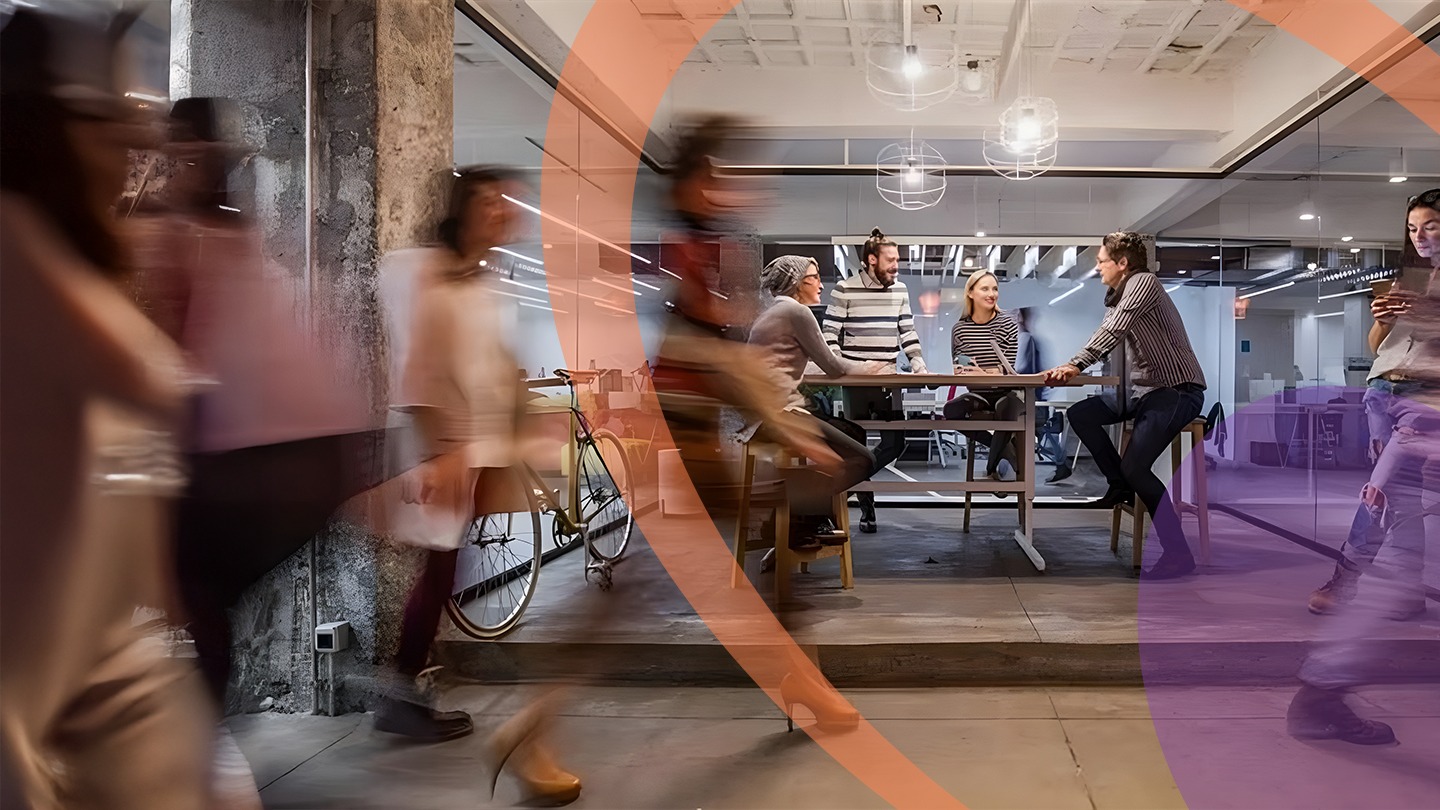 Pessoas caminhando em ambiente empresarial, pessoas sentadas numa mesa ao fundo