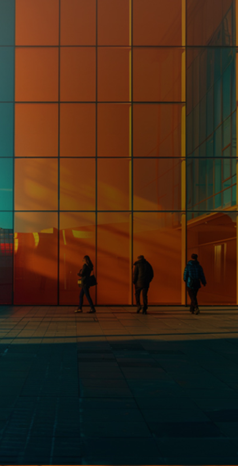 Imagem de um prédio moderno com fachadas de vidro refletindo o pôr do sol, com três pessoas caminhando na frente, ideal para arquitetura moderna.
