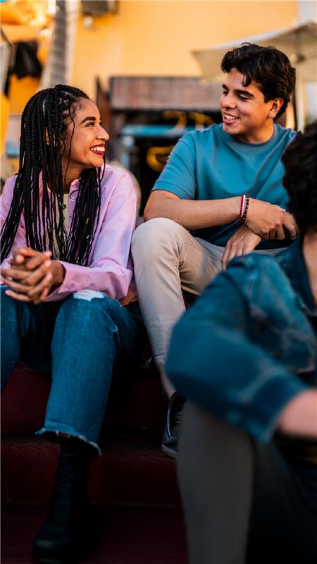 Grupo de jovens sorrindo e conversando em ambiente descontraído, demonstrando amizade e alegria em momento social feliz.