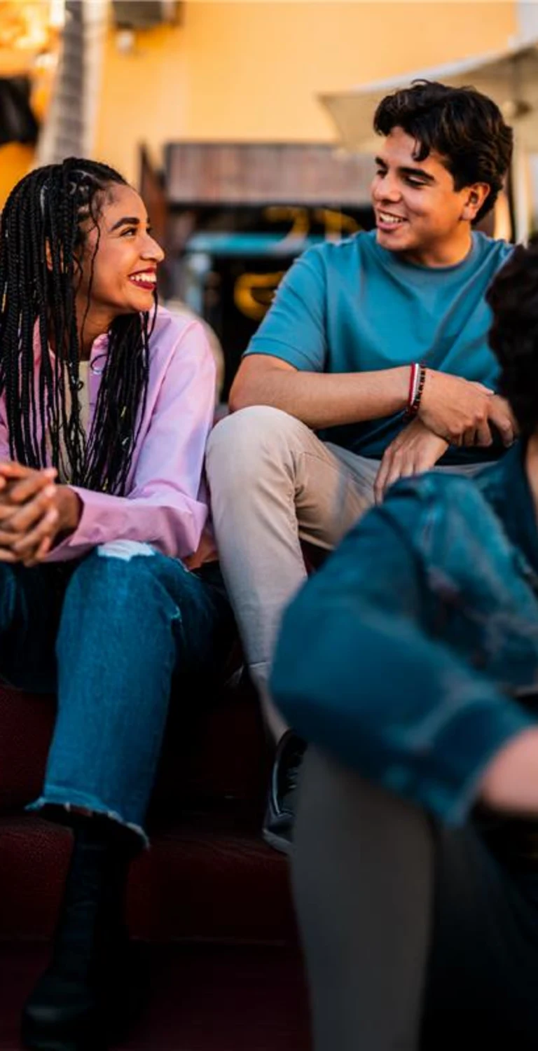 Grupo de jovens sorrindo e conversando em ambiente descontraído, demonstrando amizade e alegria em momento social feliz.