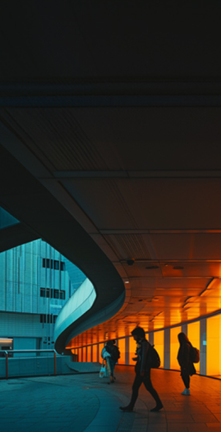Imagem de um espaço moderno com iluminação de luzes laranja e azuis, pessoas caminhando sob uma estrutura arquitetônica futurista, ideal para eventos e exposições.