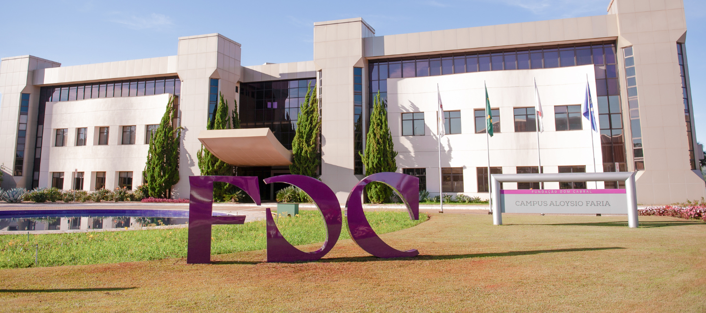 Front view of a modern educational campus building with large windows, landscaped grounds, and a prominent purple FDC sculpture on the lawn under a clear blue sky.