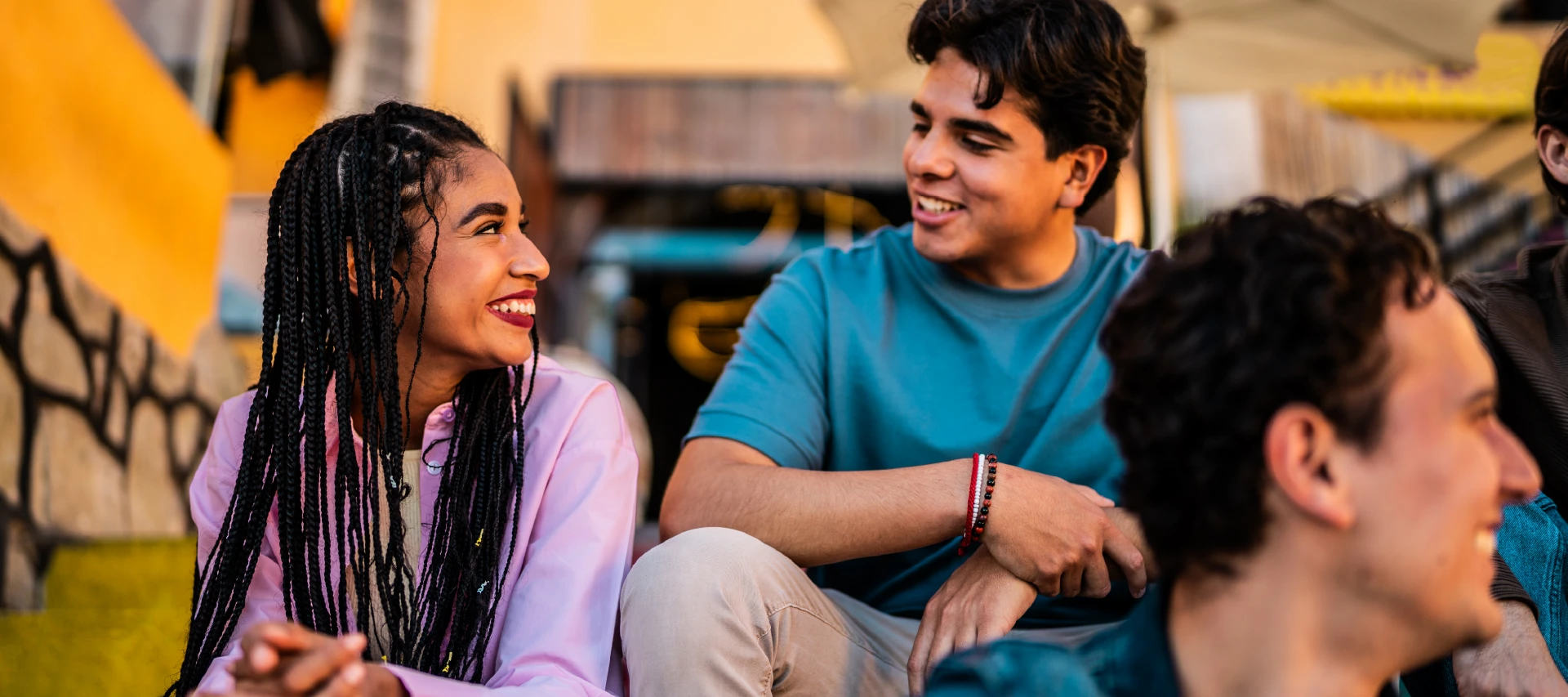 Grupo de jovens sorrindo e conversando em ambiente descontraído, demonstrando amizade e alegria em momento social feliz.