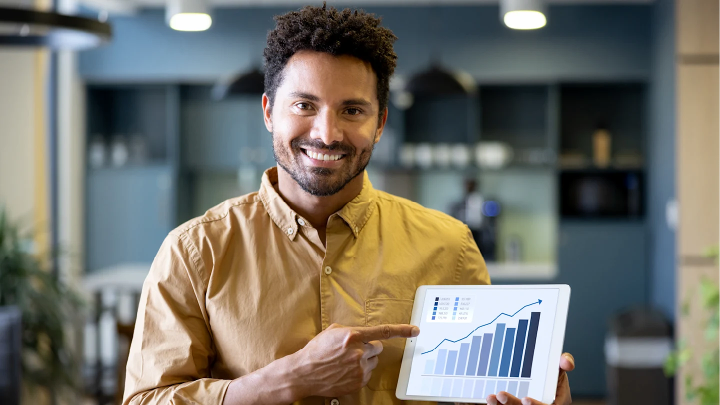 Um homem sorrindp e apontando para um gráfico em um tablet.