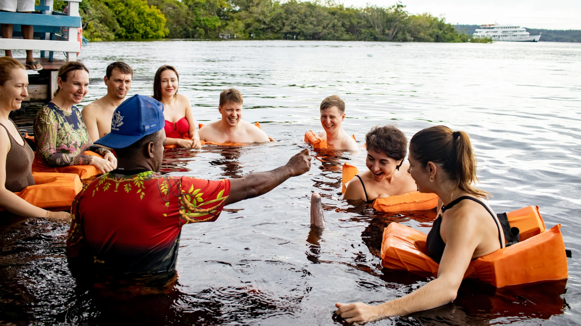 Visitors wearing life jackets participate in a river activity led by a local guide, standing in calm Amazon waters surrounded by lush tropical vegetation.