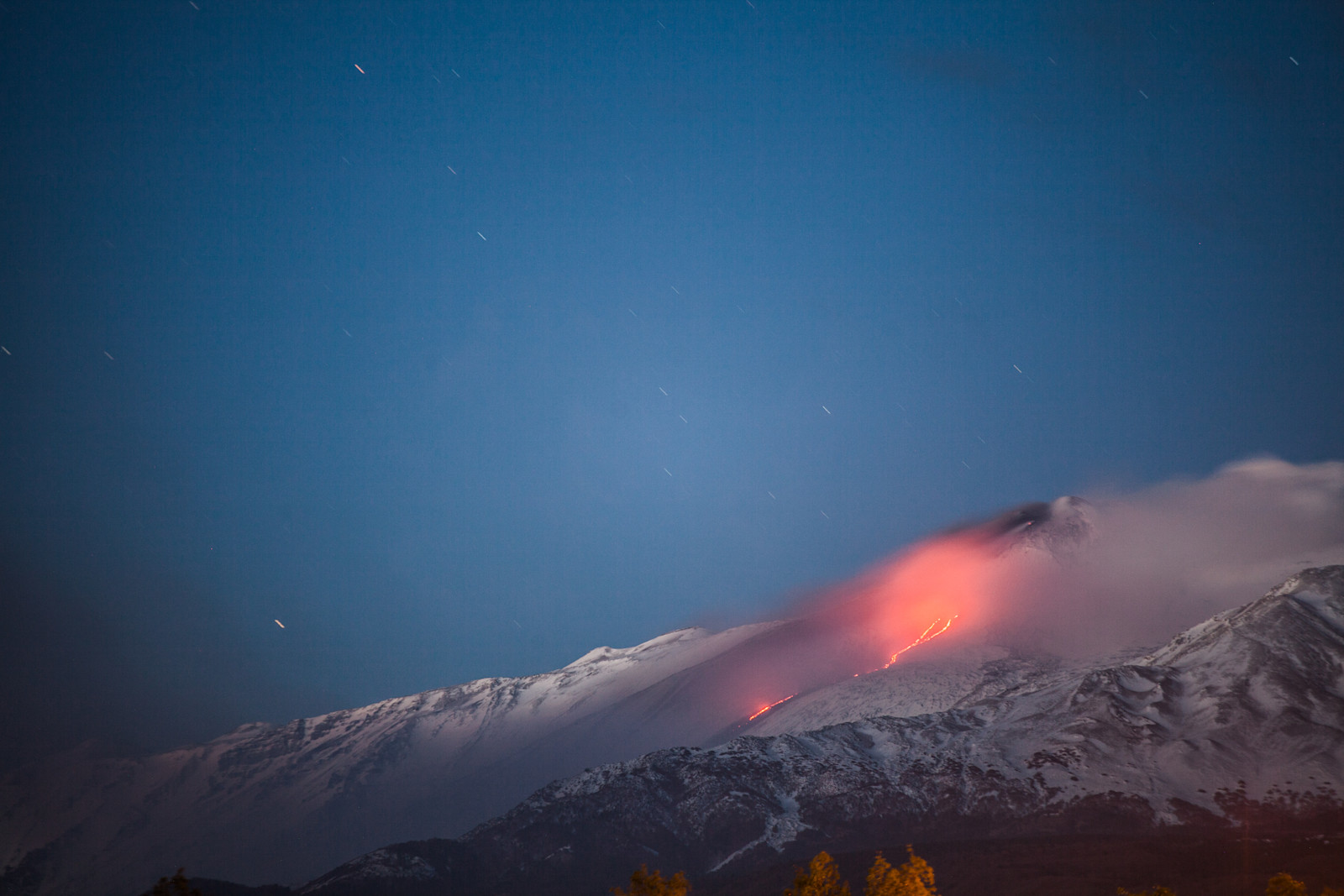Mount Etna in Italy with a lava flow at night.