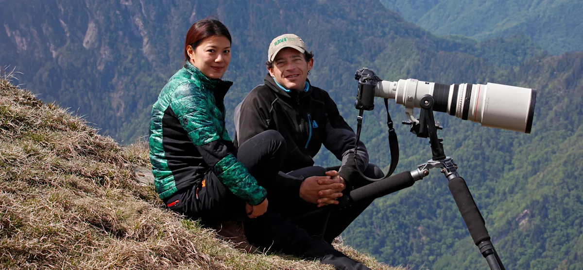 Jed Weingarten sits with camera equipment on a mountainside with forested mountains in the background.