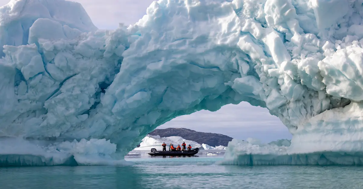 Travelers pass by, framed by an ice arch, in Sermilik Fjord, Greenland.