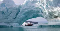Travelers pass by, framed by an ice arch, in Sermilik Fjord, Greenland.
