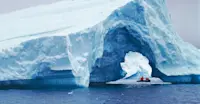Guests in Zodiac cruise past an iceberg arch, Antarctica.