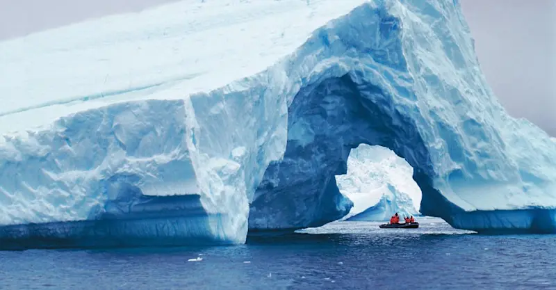 Guests in Zodiac cruise past an iceberg arch, Antarctica.
