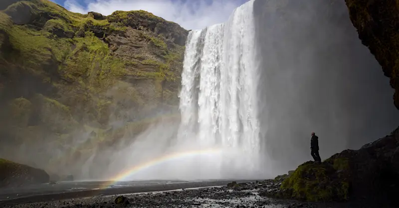 A traveler peers at the mighty Skogafoss, Iceland.
