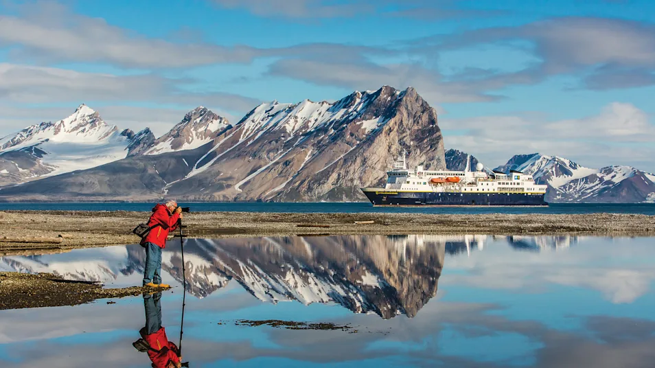 A traveler photographs the landscape in front of mountains and the National Geographic Explorer, Norway