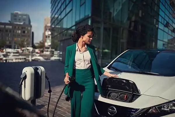 A woman in business suit charging an electric vehicle at a charging station in the city.