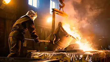 A person pouring hot molten liquid in a manfuacturing plant.