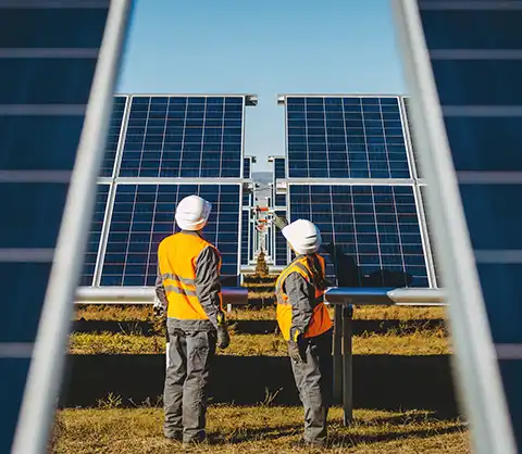 Two men looking at solar panels in open solar field against blue sky.