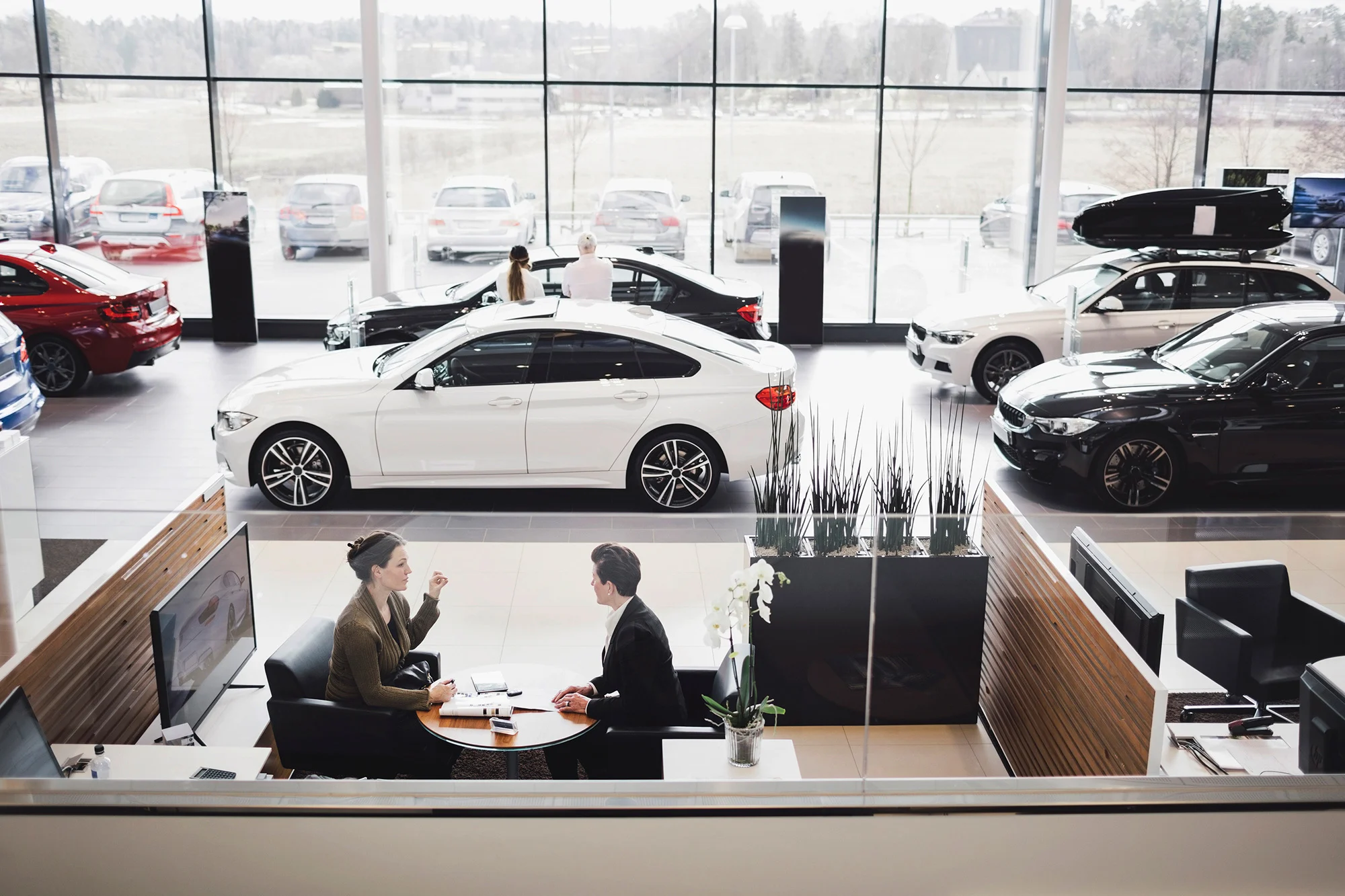 Two people having a conversation with several cars in the background at a Penske facility