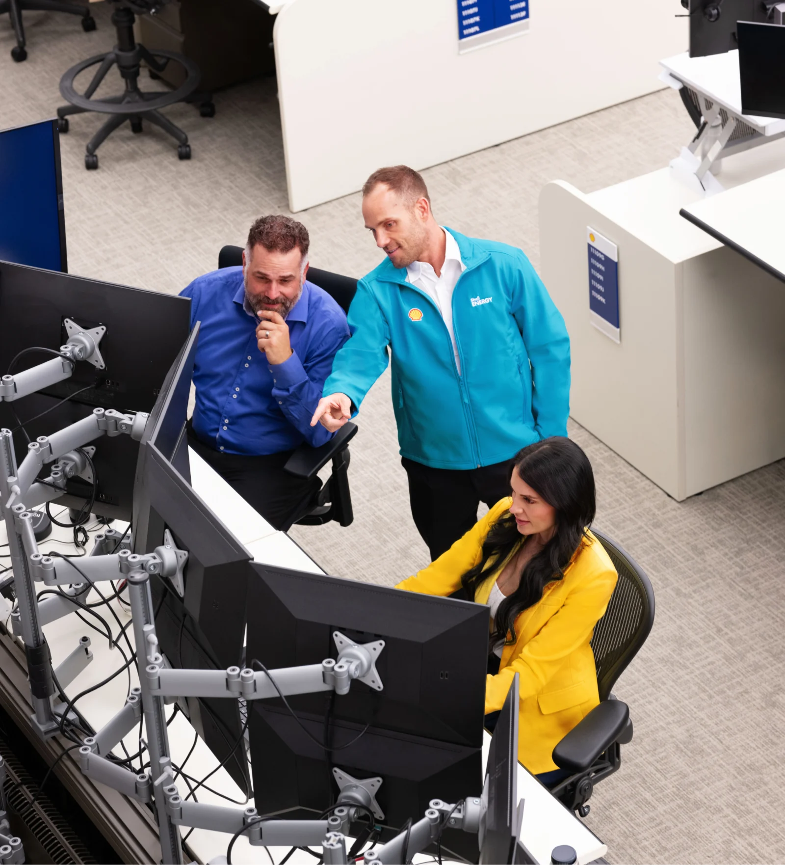 A man, woman, and Shell representative looking at a computer on a business trading floor.