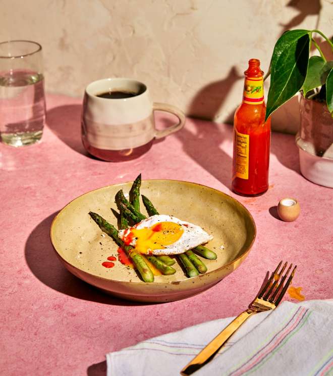Grilled asparagus on plate with runny olive-oil-fried sunny side up egg and hot sauce