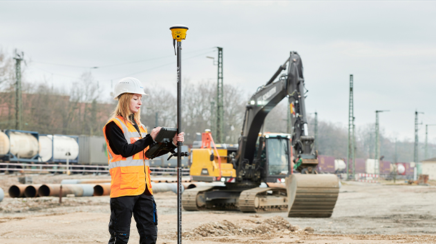 Worker on site using GNSS Smart Antenna on construction site with excavator