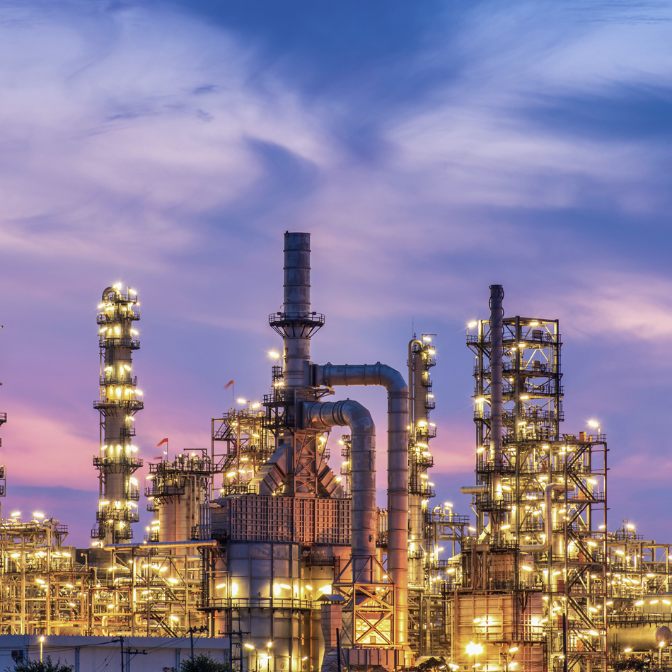 夕阳映照下的炼油厂全景，高耸的烟囱阵列与银色储罐群构成主体画面。