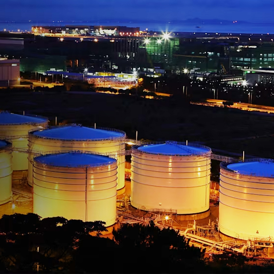Vue nocturne des réservoirs de pétrole illuminés par les lumières de la ville, mettant en valeur un paysage industriel