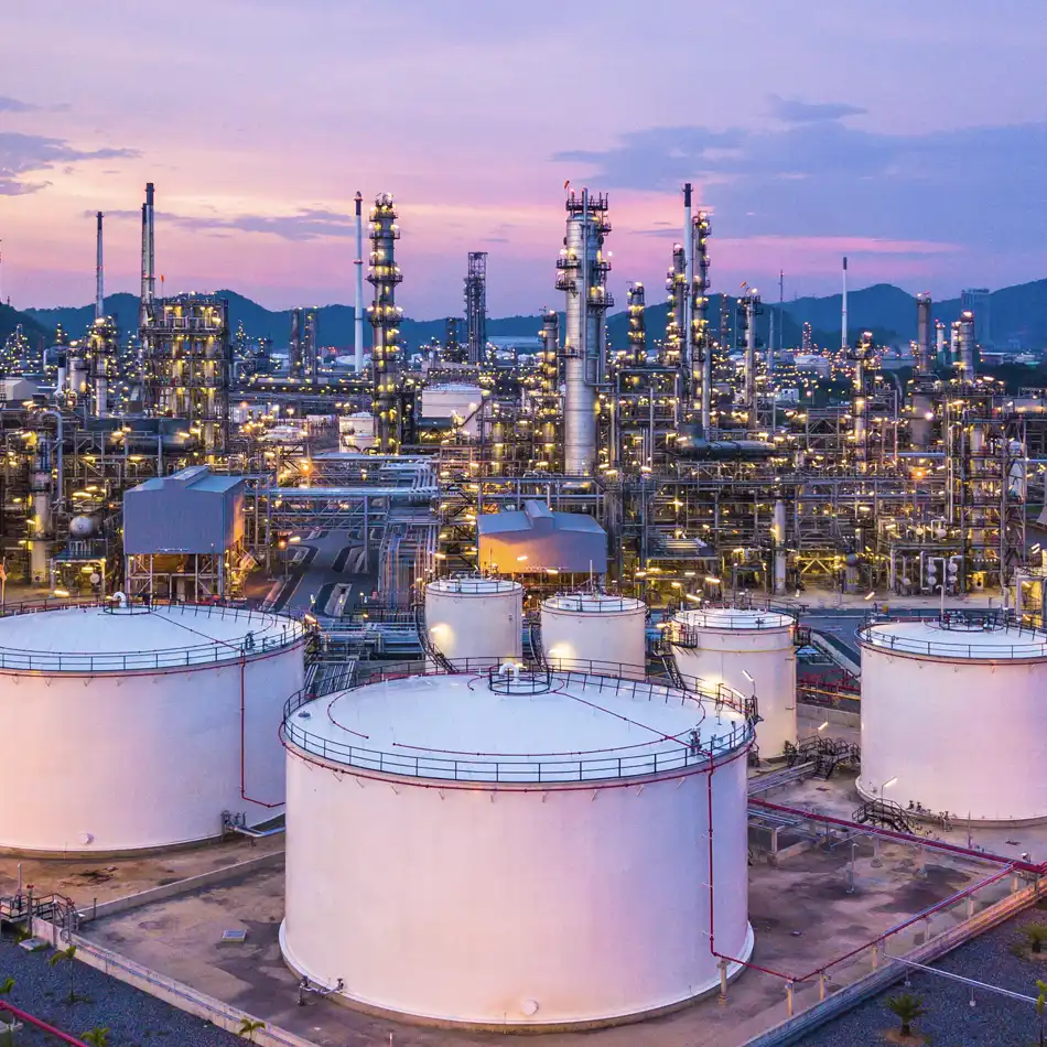 Oil refinery silhouetted against a vibrant sunset, with smoke rising from chimneys