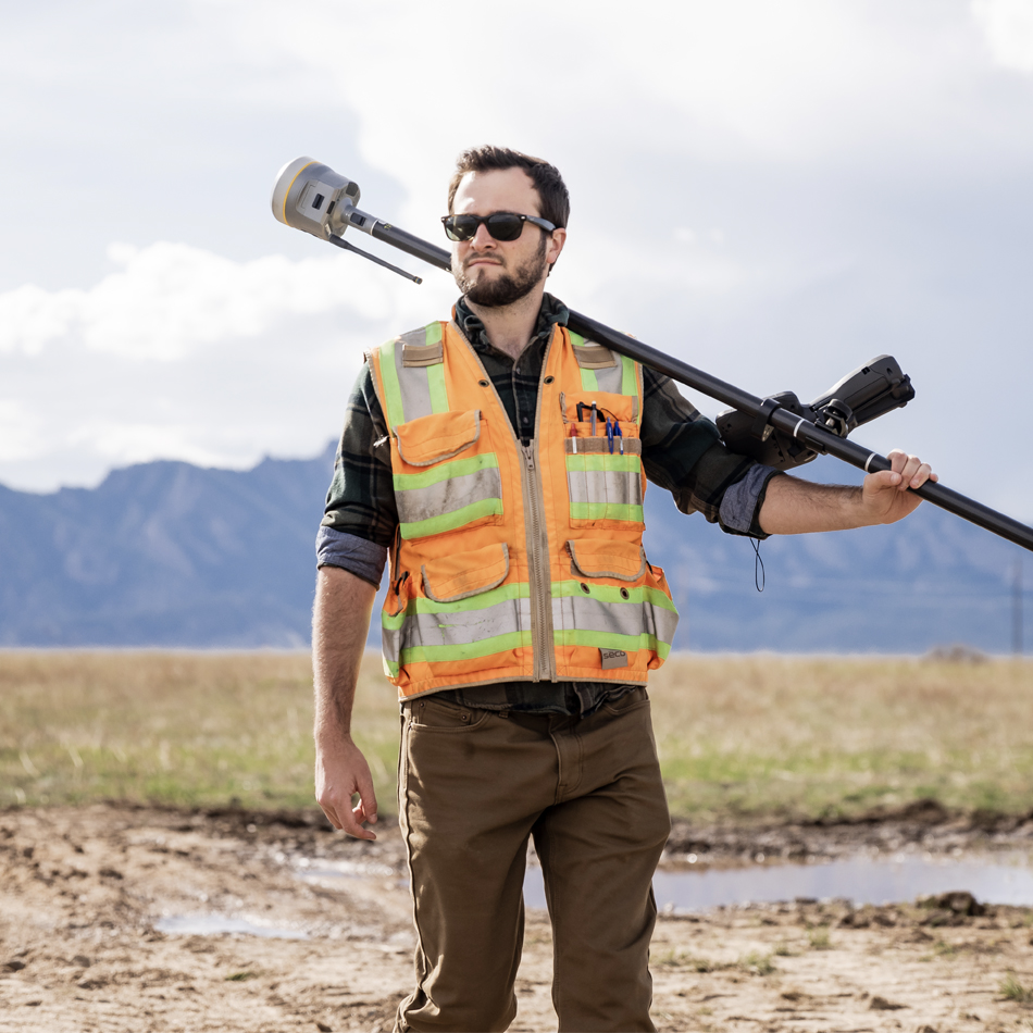 身着反光背心的测绘人员携行 Trimble R980 GNSS 接收机