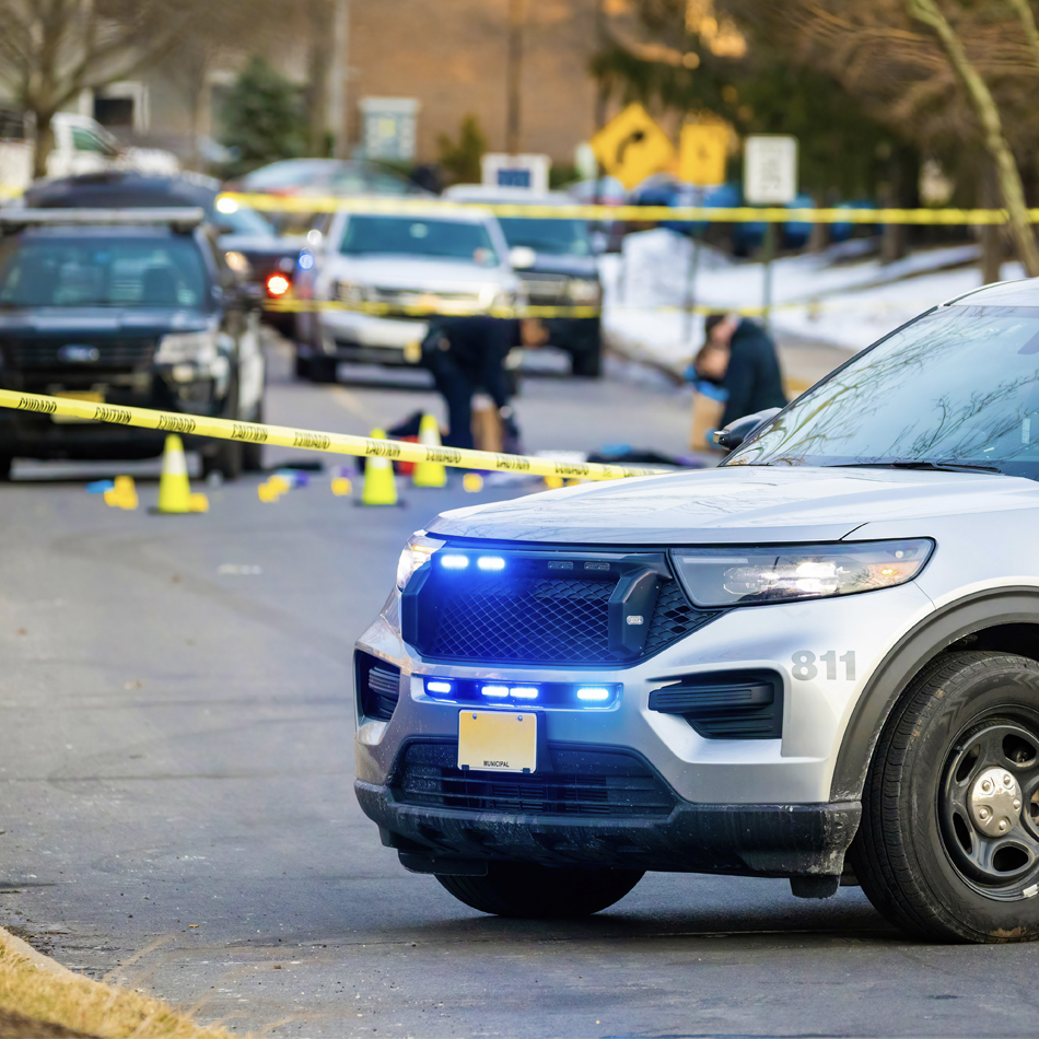 A police vehicle parked in front of yellow police tape, indicating a secured area for an ongoing investigation