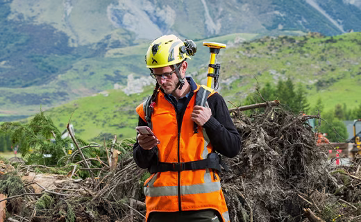 Forestry worker with Trimble DA2 on a backpack and mountain range in the background.