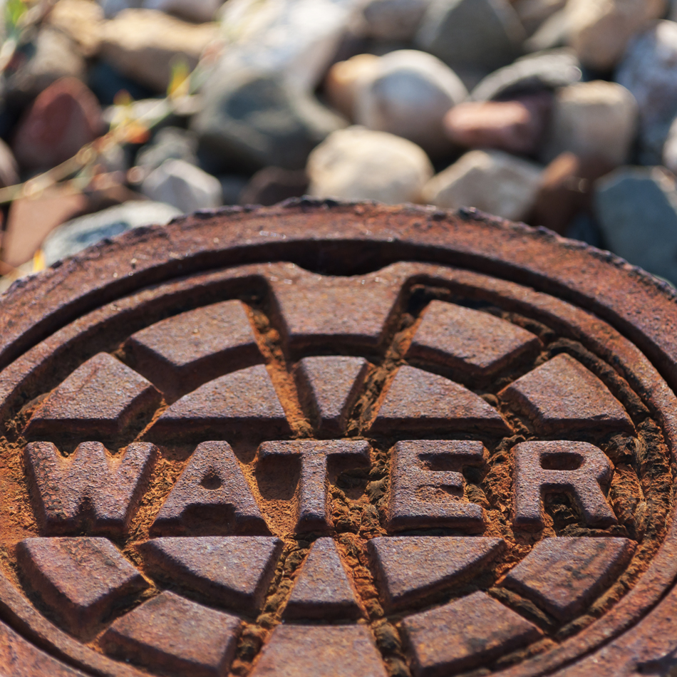 A close-up of a rusty manhole cover featuring the word "water."
