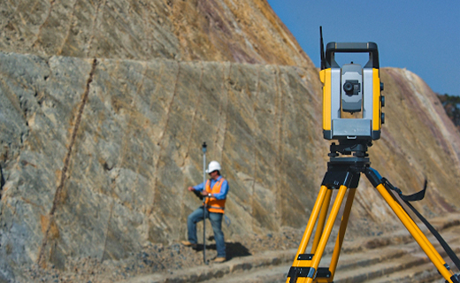 Mining worker measuring a mining stockpile, with a Trimble total station in foreground