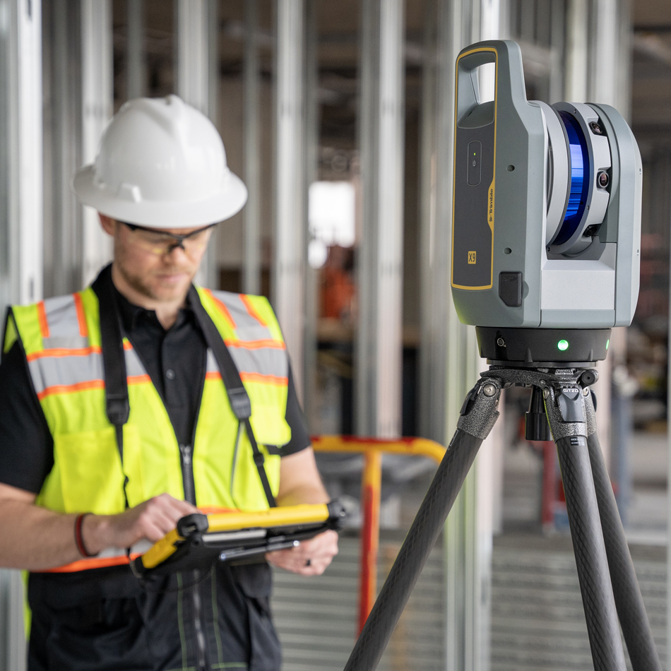 Worker in vest and hard hat using Trimble X9 laser scanner at a building construction site