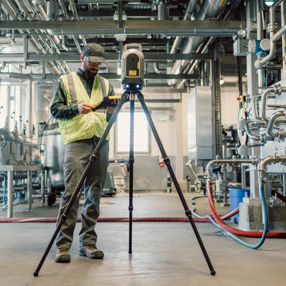 Worker in a yellow vest testing a Trimble X9 laser scanner set on a tripod.