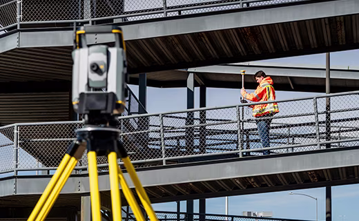 A surveyor operates a Trimble T70 tablet attached to a pole equipped with a 360-degree prism.