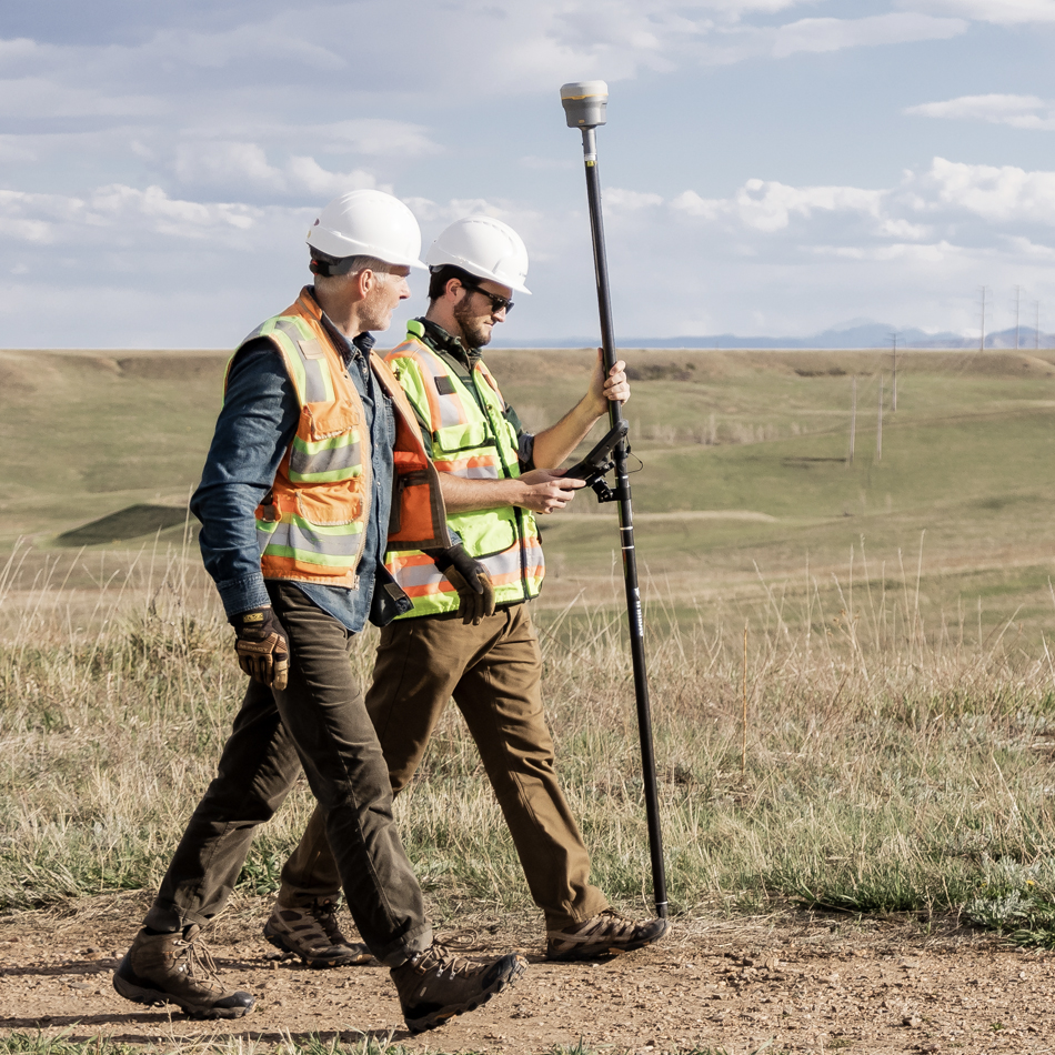 Deux géomètres portant des gilets qui marchent en tenant un système GNSS Trimble R980