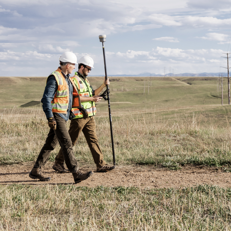Two surveyors with vests walk around with a Trimble R980 GNSS system