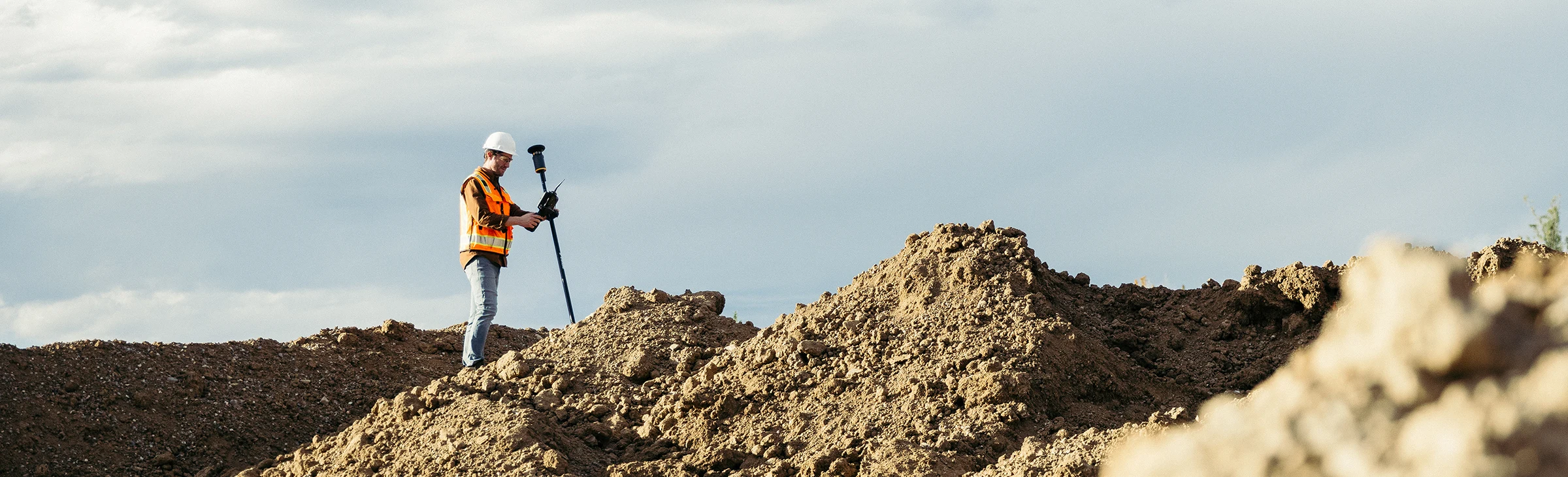 Man in construction safety gear standing on a big dirt hill, programming a tablet and a Trimble ST30 smart target.